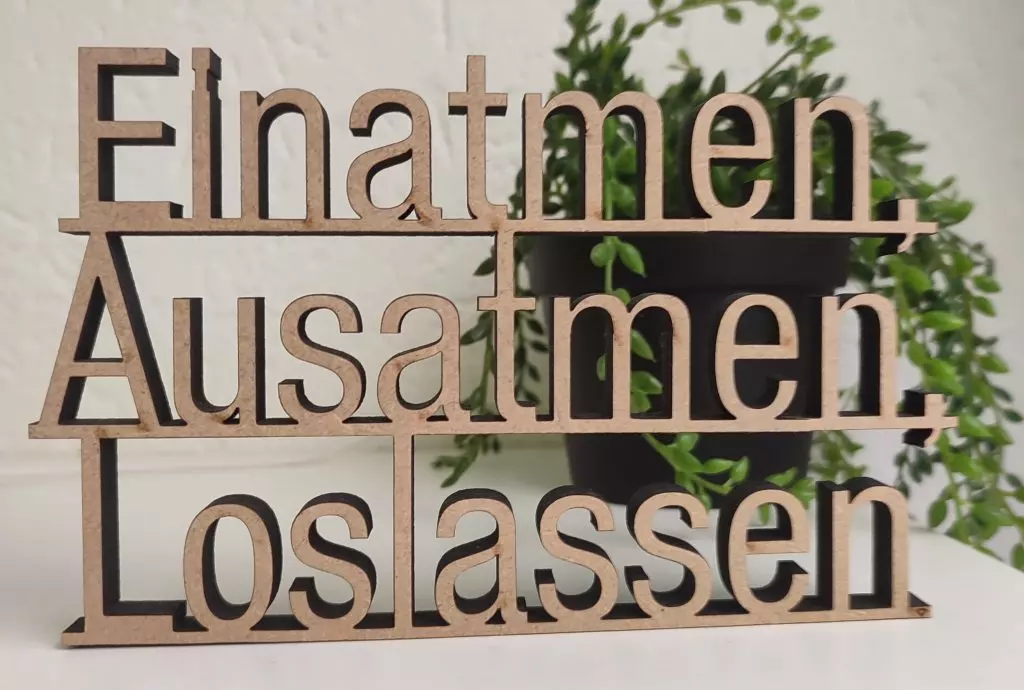 Holzschriftzug "Einatmen, Ausatmen, Loslassen" vor einer grünen Pflanze, Symbolbild für den Entspannungsabend "Entspannung pur" in der ImpulsQuelle